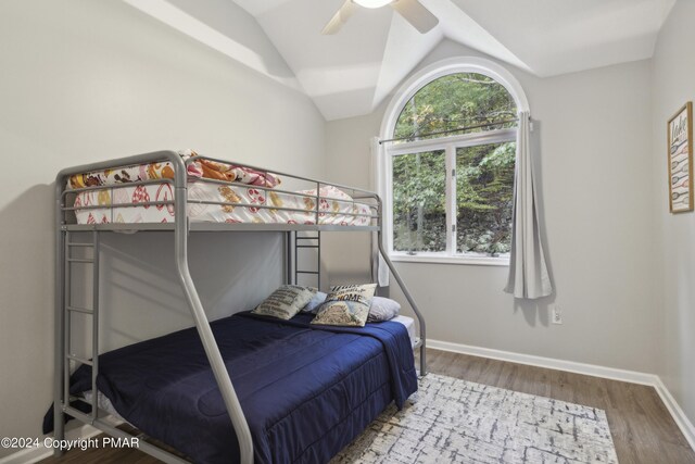 bedroom featuring lofted ceiling, multiple windows, baseboards, and wood finished floors