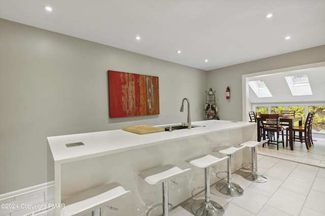 kitchen featuring a skylight, light tile patterned floors, a breakfast bar, a sink, and recessed lighting