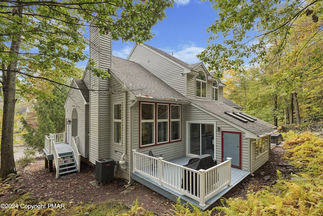 back of house featuring a wooden deck, a chimney, central AC unit, and roof with shingles