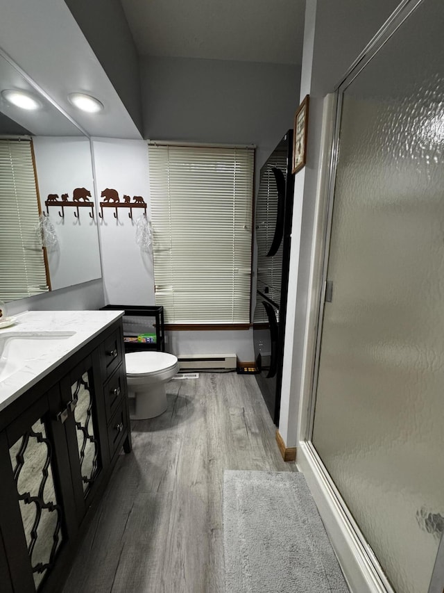 bathroom featuring wood finished floors, baseboard heating, vanity, and a stall shower