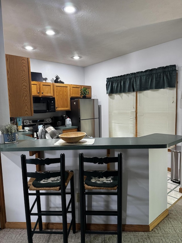kitchen featuring appliances with stainless steel finishes, dark countertops, light carpet, a kitchen breakfast bar, and a textured ceiling