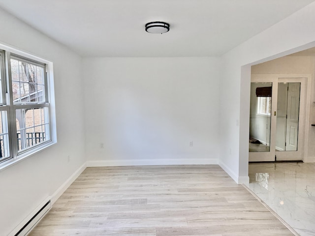 empty room featuring a baseboard heating unit, light wood-style flooring, and baseboards