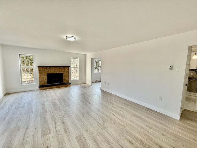 unfurnished living room featuring a fireplace with raised hearth, light wood-type flooring, a baseboard radiator, and baseboards