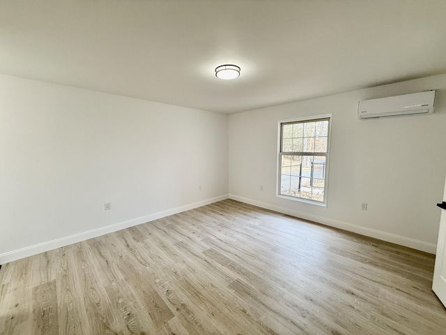 unfurnished room featuring light wood finished floors, a wall unit AC, and baseboards