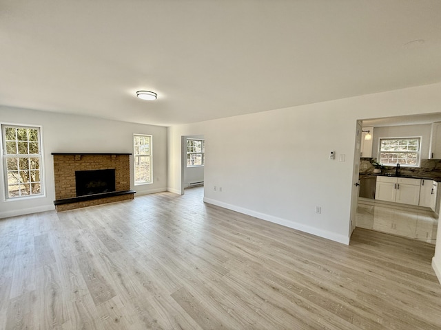 unfurnished living room featuring a fireplace with raised hearth, light wood-type flooring, a sink, and baseboards