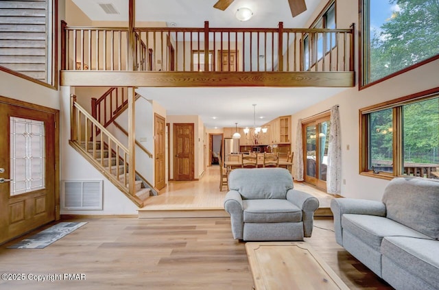 living room with a high ceiling, ceiling fan with notable chandelier, and light hardwood / wood-style floors