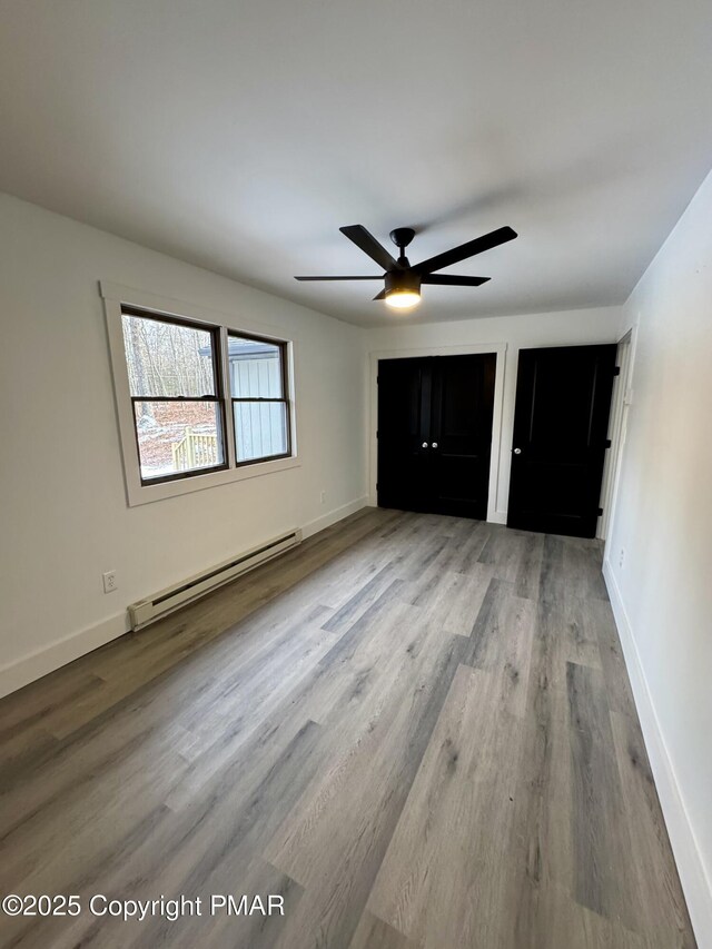 unfurnished bedroom with a baseboard heating unit, ceiling fan, baseboards, and wood finished floors