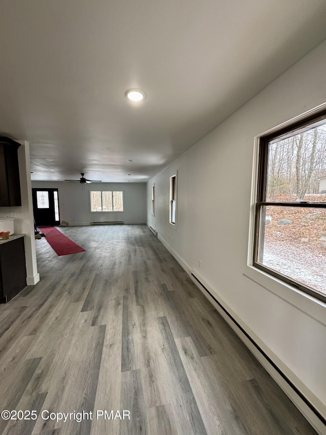 unfurnished living room featuring ceiling fan, baseboard heating, wood finished floors, and baseboards