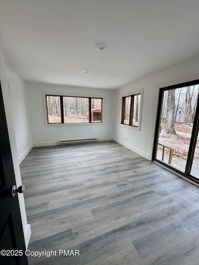 empty room featuring baseboard heating, plenty of natural light, wood finished floors, and baseboards