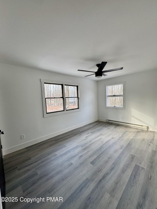 unfurnished room with a baseboard heating unit, a ceiling fan, baseboards, and dark wood-style floors