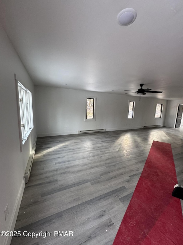 unfurnished living room featuring baseboards, a baseboard heating unit, and wood finished floors