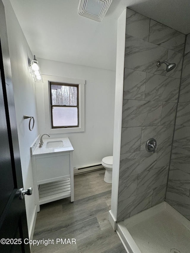 bathroom featuring toilet, baseboard heating, a tile shower, vanity, and wood finished floors