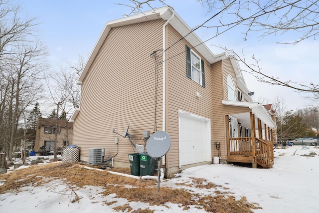 view of snowy exterior featuring an attached garage and central AC unit