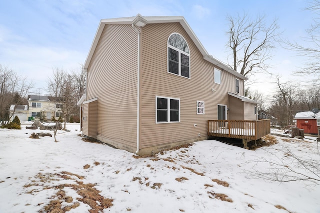 snow covered rear of property featuring a garage and a wooden deck