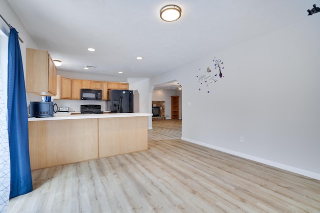 kitchen with light brown cabinetry, open floor plan, light wood-type flooring, a peninsula, and black appliances