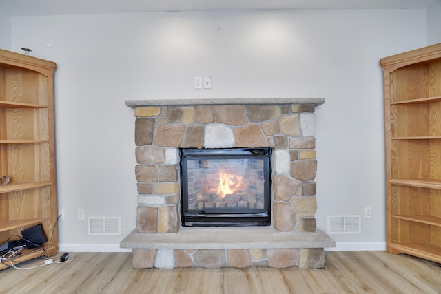 interior details with baseboards, visible vents, wood finished floors, and a stone fireplace