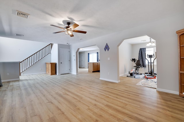 unfurnished living room featuring light wood-style floors, a ceiling fan, visible vents, and stairs