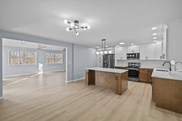 kitchen featuring a kitchen island, a sink, open floor plan, stainless steel appliances, and light wood-style flooring
