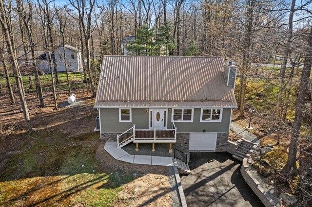 back of property featuring a garage, a chimney, concrete driveway, and metal roof