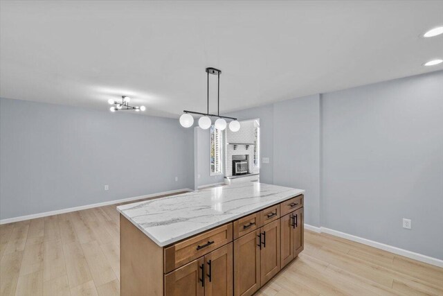 kitchen featuring decorative light fixtures, open floor plan, a brick fireplace, and light wood-style flooring