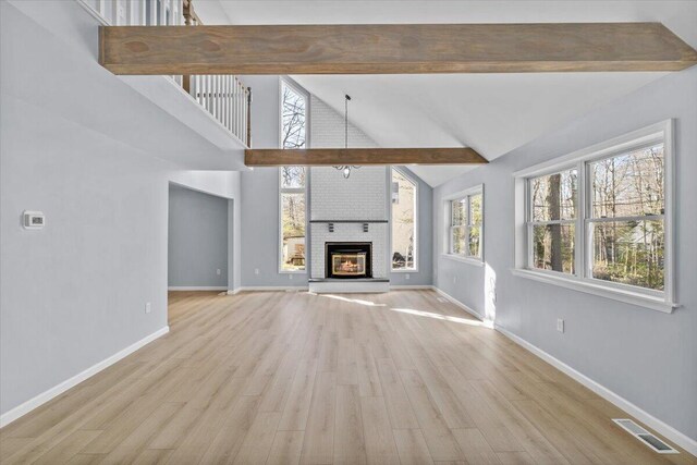 unfurnished living room with visible vents, a brick fireplace, beam ceiling, baseboards, and light wood-style flooring
