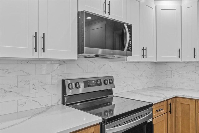 kitchen with backsplash, stainless steel appliances, white cabinets, and light stone counters