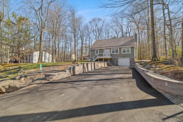 view of front of property with stone siding, a garage, stairway, a chimney, and driveway