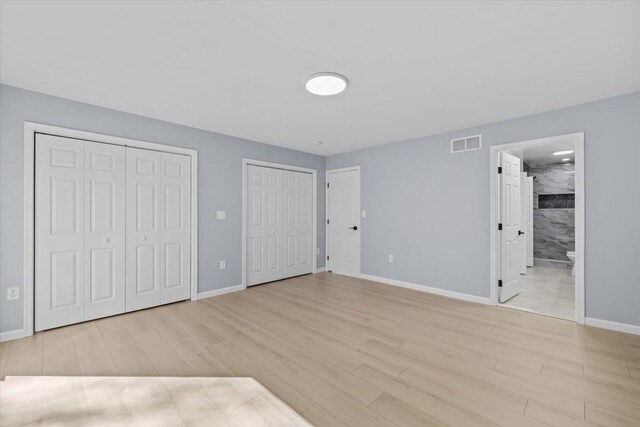 unfurnished bedroom featuring multiple closets, visible vents, baseboards, and light wood-type flooring