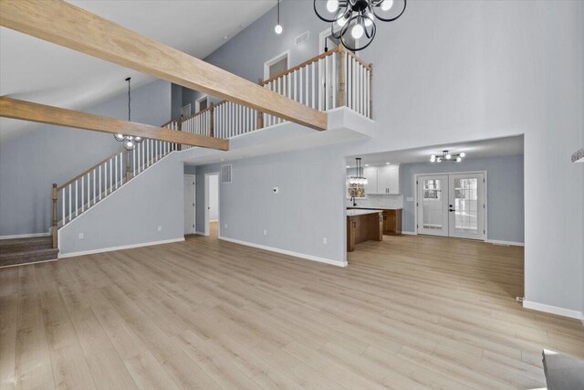 unfurnished living room with a notable chandelier, high vaulted ceiling, baseboards, light wood-type flooring, and stairway