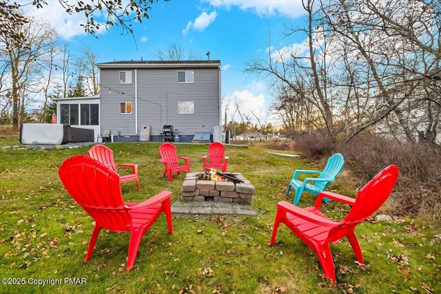 back of property with a sunroom, a yard, and an outdoor fire pit