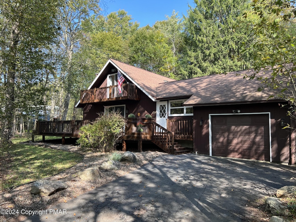 chalet / cabin featuring a deck, aphalt driveway, roof with shingles, and an attached garage