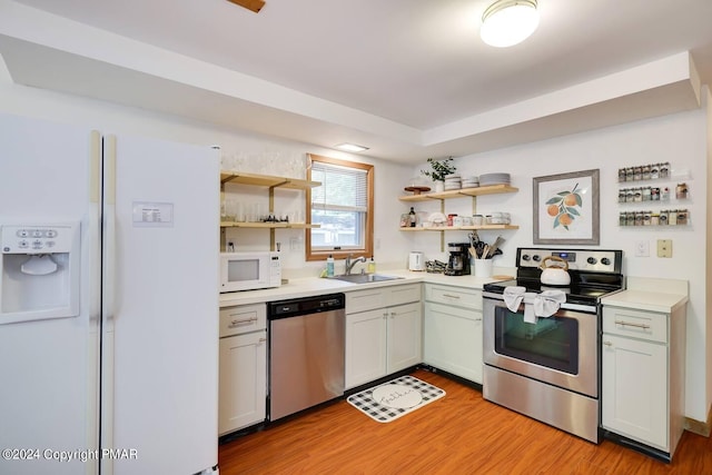 kitchen with open shelves, stainless steel appliances, light countertops, light wood-style floors, and a sink