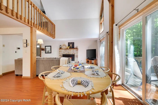 dining room featuring baseboards, a fireplace, a towering ceiling, and light wood finished floors