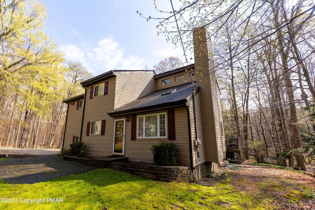 view of front of property with a front yard, roof with shingles, driveway, and a chimney