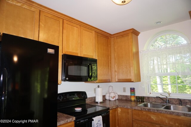 kitchen featuring dark countertops, black appliances, brown cabinetry, and a sink