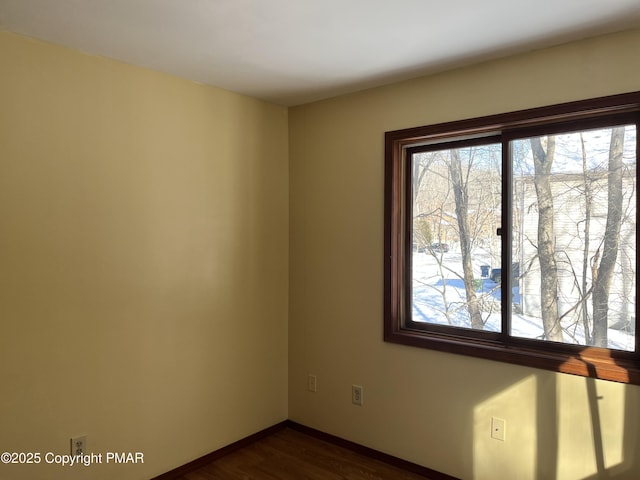 spare room with baseboards and dark wood-type flooring