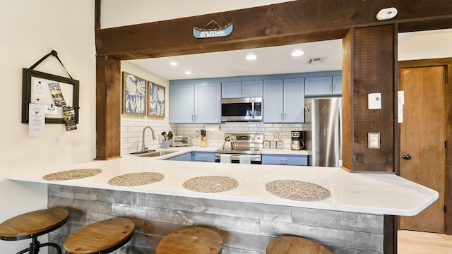 kitchen with a breakfast bar, a peninsula, a sink, appliances with stainless steel finishes, and tasteful backsplash