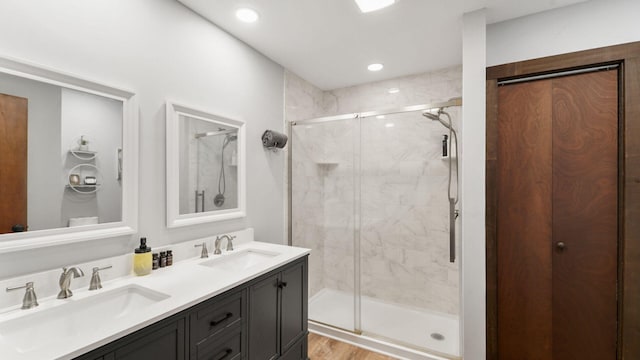 full bath with a sink, double vanity, wood finished floors, and a shower stall