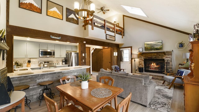 dining room featuring a skylight, a stone fireplace, light wood-style flooring, and an inviting chandelier