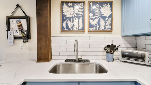 kitchen featuring light stone countertops, blue cabinetry, a toaster, a sink, and decorative backsplash