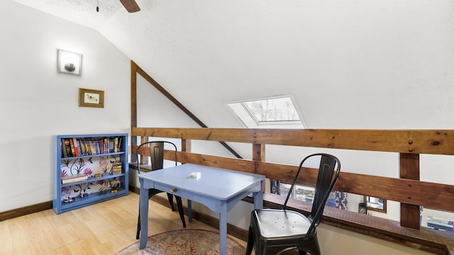 home office with light wood-type flooring, a ceiling fan, a textured ceiling, vaulted ceiling with skylight, and baseboards