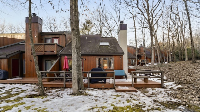 snow covered rear of property with a deck and a chimney