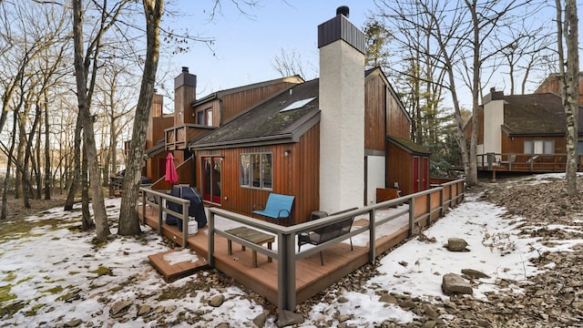 snow covered rear of property featuring a wooden deck and a chimney