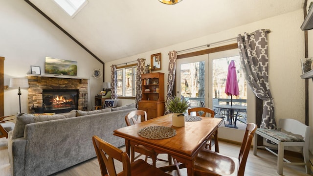 dining room featuring high vaulted ceiling, a fireplace, a skylight, and light wood-style floors