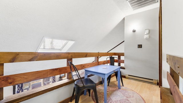 office area with a baseboard heating unit, vaulted ceiling with skylight, visible vents, and wood finished floors