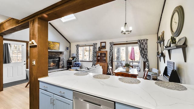 kitchen featuring light stone counters, a fireplace, vaulted ceiling, dishwasher, and open floor plan