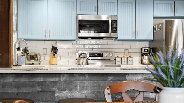 kitchen with a sink, stainless steel microwave, blue cabinets, and decorative backsplash