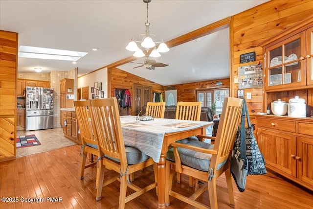 dining room with lofted ceiling, wood walls, light wood-style flooring, and ceiling fan