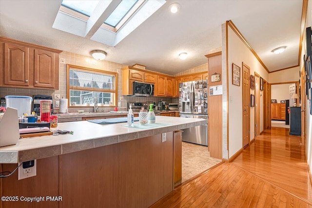 kitchen featuring vaulted ceiling with skylight, a peninsula, stainless steel appliances, light wood-style floors, and backsplash