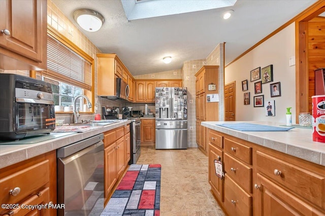 kitchen with a sink, vaulted ceiling, appliances with stainless steel finishes, decorative backsplash, and brown cabinetry